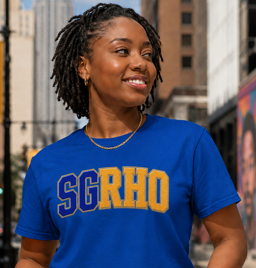 Woman wearing a blue t-shirt with 'SGRHO' in yellow and blue letters, standing on a city street.